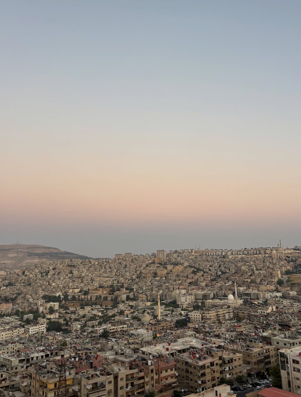 A city spread over hills at dusk under a pink sky